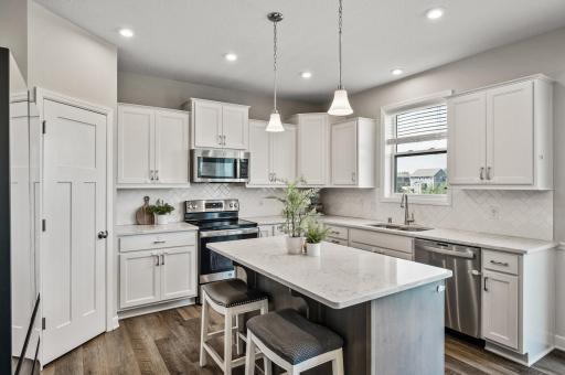 Beautiful bright kitchen with quartz counters, tile backsplash, ss appliances, walk in pantry, and park views.