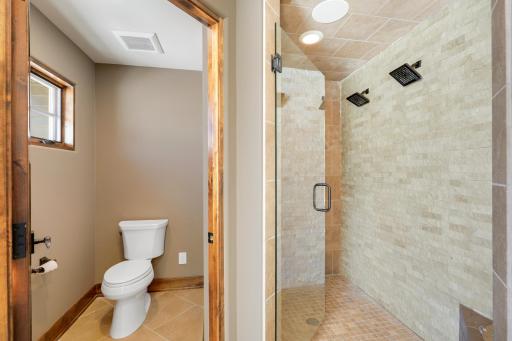 Retire to the luxurious primary ensuite with panoramic lake views, vaulted ceilings, natural stone-topped vanity with dual sinks, a soaker tub, a walk-in shower with two shower heads, and a huge walk-in closet.