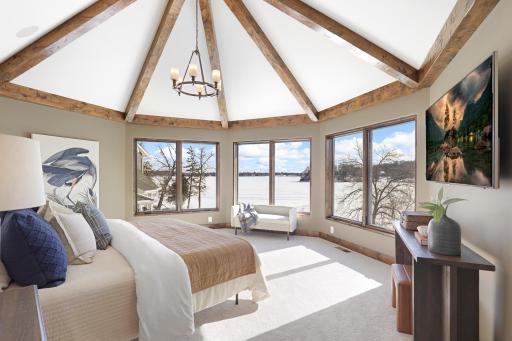 Retire to the luxurious primary ensuite with panoramic lake views, vaulted ceilings, natural stone-topped vanity with dual sinks, a soaker tub, a walk-in shower with two shower heads, and a huge walk-in closet.