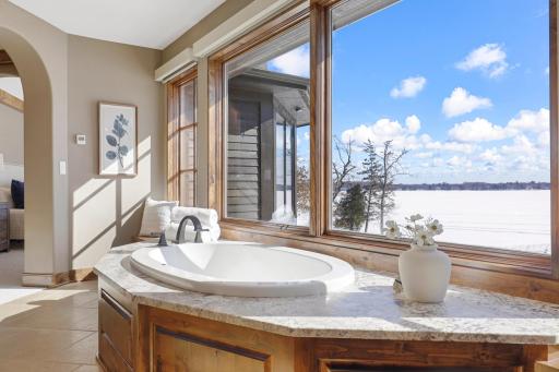 Retire to the luxurious primary ensuite with panoramic lake views, vaulted ceilings, natural stone-topped vanity with dual sinks, a soaker tub, a walk-in shower with two shower heads, and a huge walk-in closet.