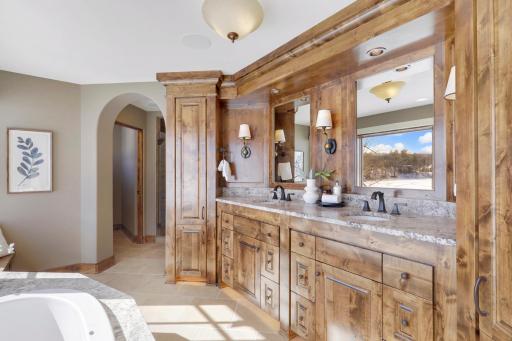 Retire to the luxurious primary ensuite with panoramic lake views, vaulted ceilings, natural stone-topped vanity with dual sinks, a soaker tub, a walk-in shower with two shower heads, and a huge walk-in closet.