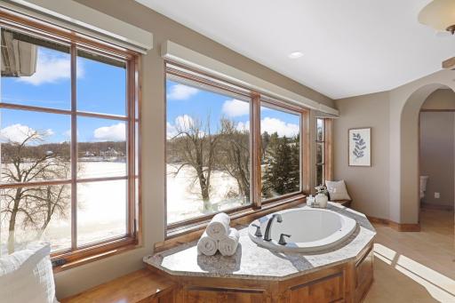 Retire to the luxurious primary ensuite with panoramic lake views, vaulted ceilings, natural stone-topped vanity with dual sinks, a soaker tub, a walk-in shower with two shower heads, and a huge walk-in closet.