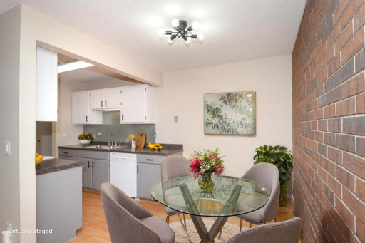 This stylish kitchen and dining area features modern two-tone cabinetry, sleek countertops, updated lighting and flooring, and a striking brick accent wall—creating an inviting space perfect for everyday living and entertaining.