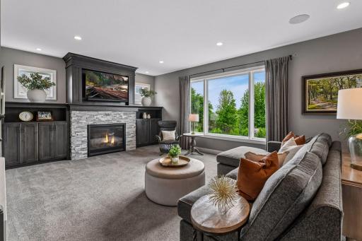 Large open family room is anchored by a gas fireplace flanked by custom built-ins, big windows overlooking private backyard pulling in afternoon light.