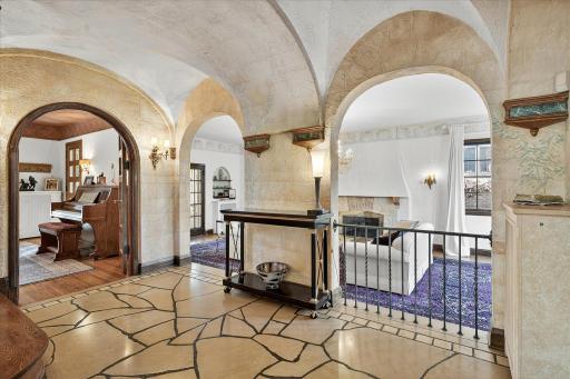 Large entryway with limestone tiled floors, vaulted arches, and hand painted plaster walls, overlooks huge sunken living room.