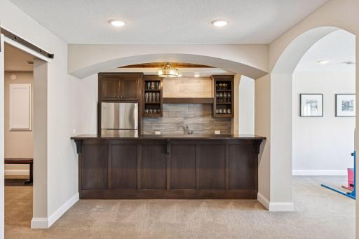 Kitchenette / Bar with granite countertops, tile backsplash, full-size refrigerator, microwave, sink, bar-height seating, and glass display cabinetry. Ideal for movie nights, entertaining, or just simply relaxing.
