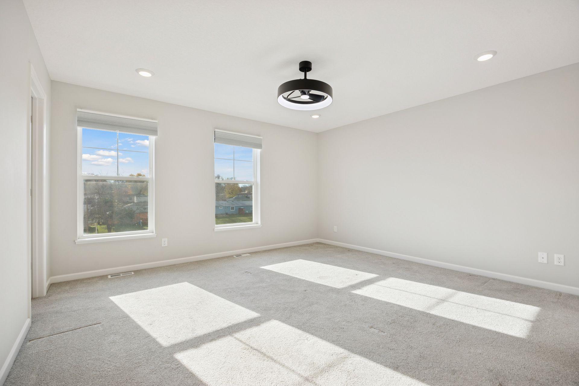 Upper level spacious primary bedroom with large windows for natural light, soft carpet and a modern ceiling fan. Plenty of room for a king-size bed and sitting area.
