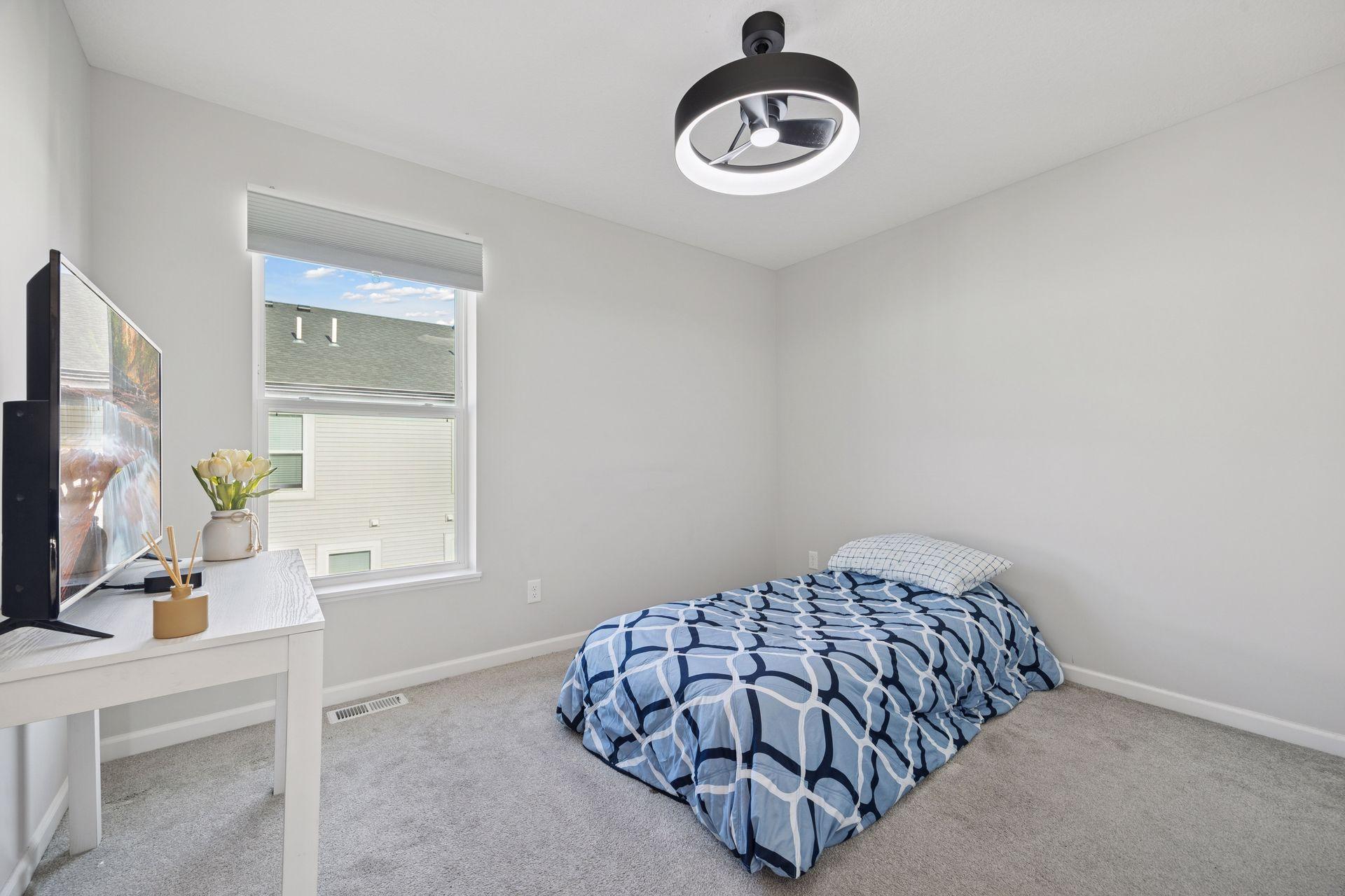Upper level comfortable second bedroom with soft carpeting, a large window, and modern light fixture - perfect for a guest room or office
