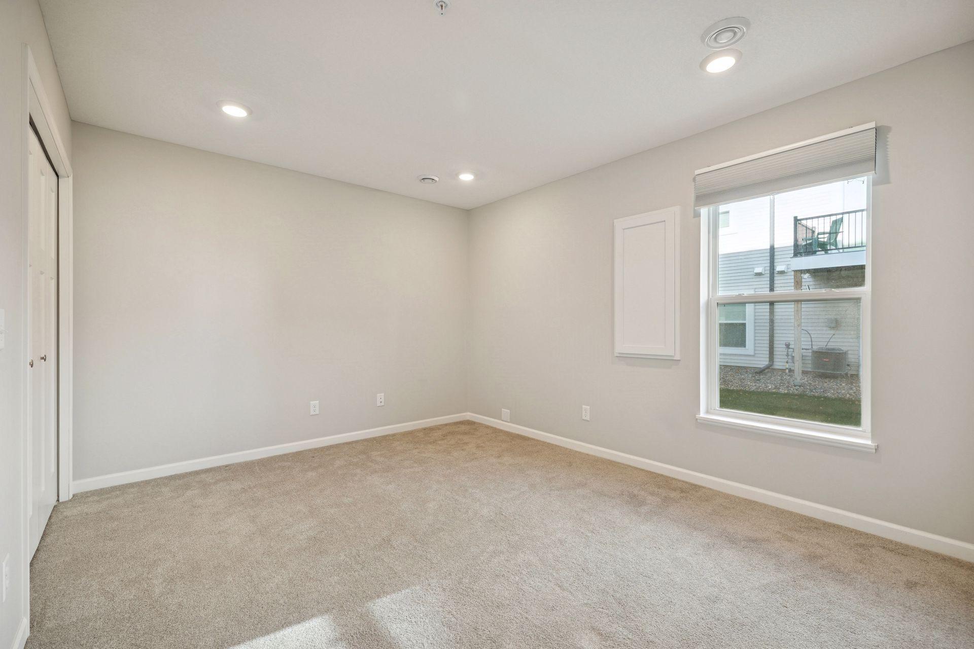 The lower-level family room featuring soft carpet, neutral walls and a bright window. This flexible space connects easily to the walk-out area -great for a guest room, office or media space.
