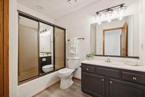 Updated full bathroom featuring a modern vanity, new lighting, and tub with sliding glass doors.