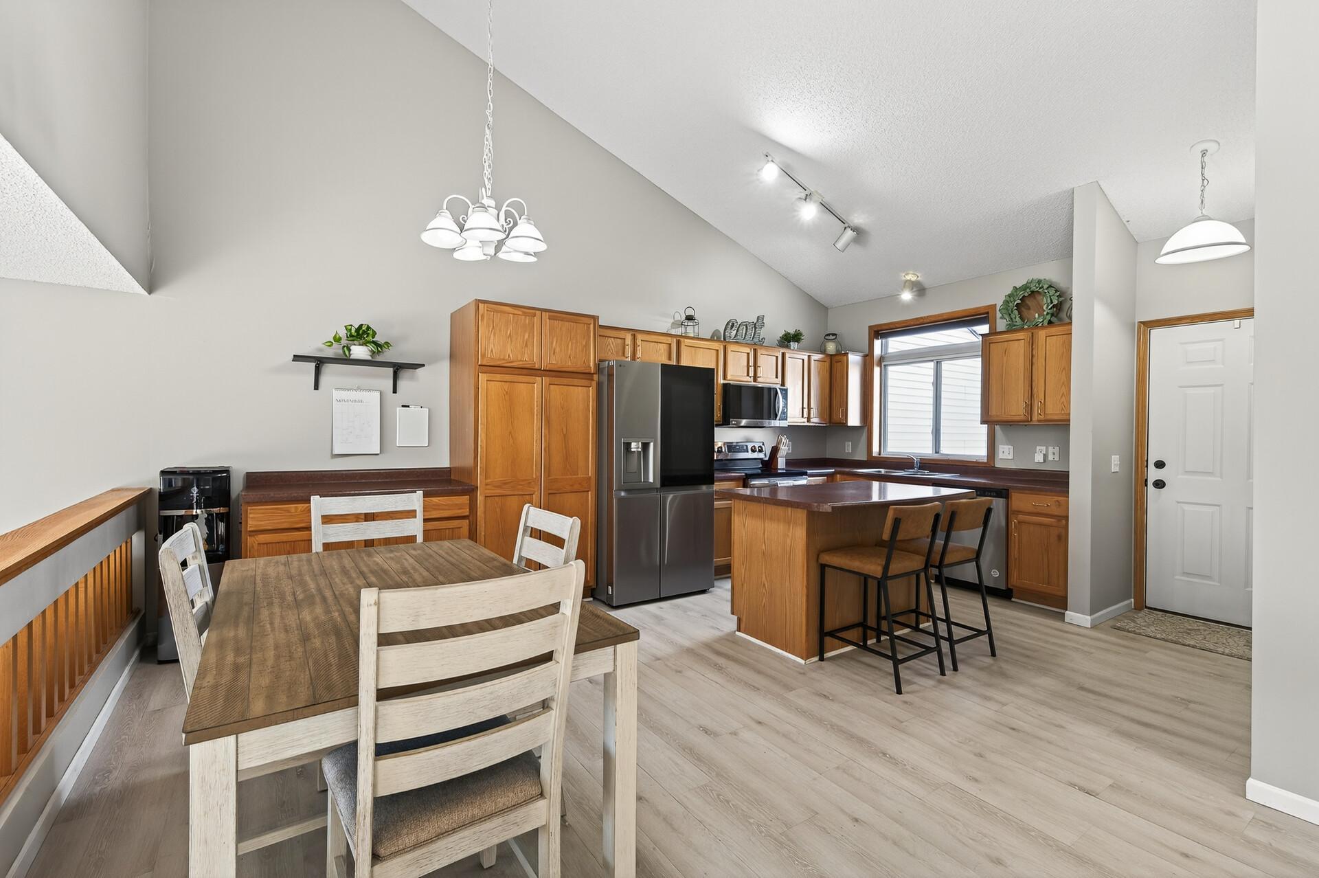 Bright, open kitchen and dining area with vaulted ceilings, updated flooring, stainless steel appliances, center island seating, and great natural light.