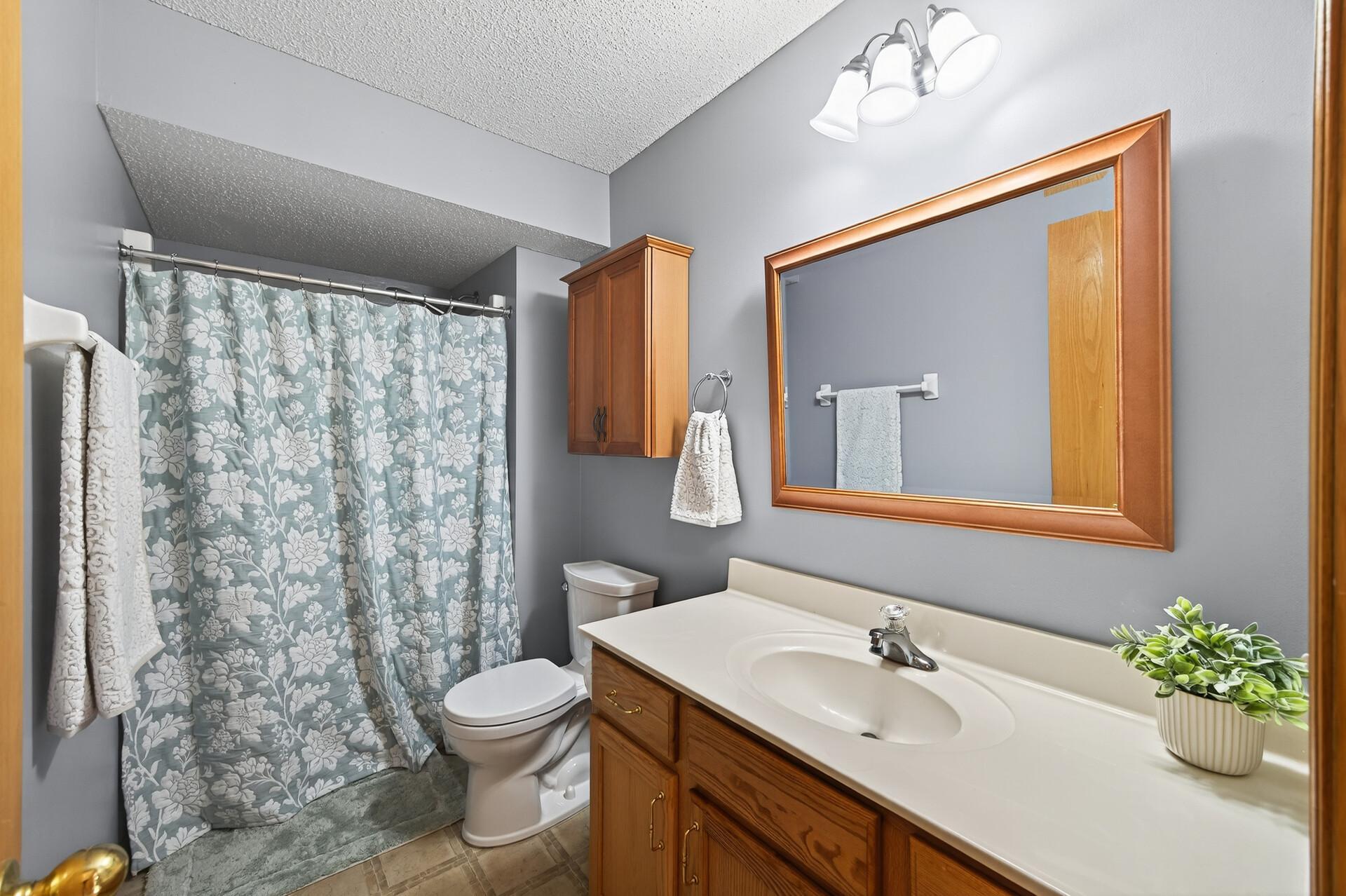 Full bath with tub/shower combo, extended vanity, updated lighting, and warm wood cabinetry.