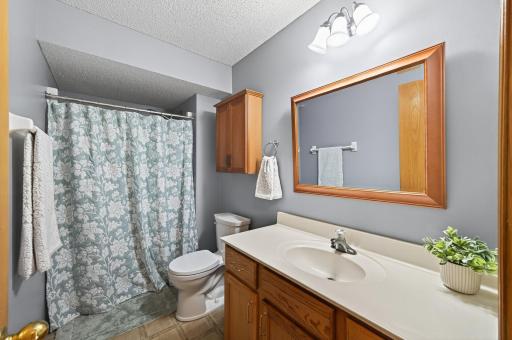 Full bath with tub/shower combo, extended vanity, updated lighting, and warm wood cabinetry.