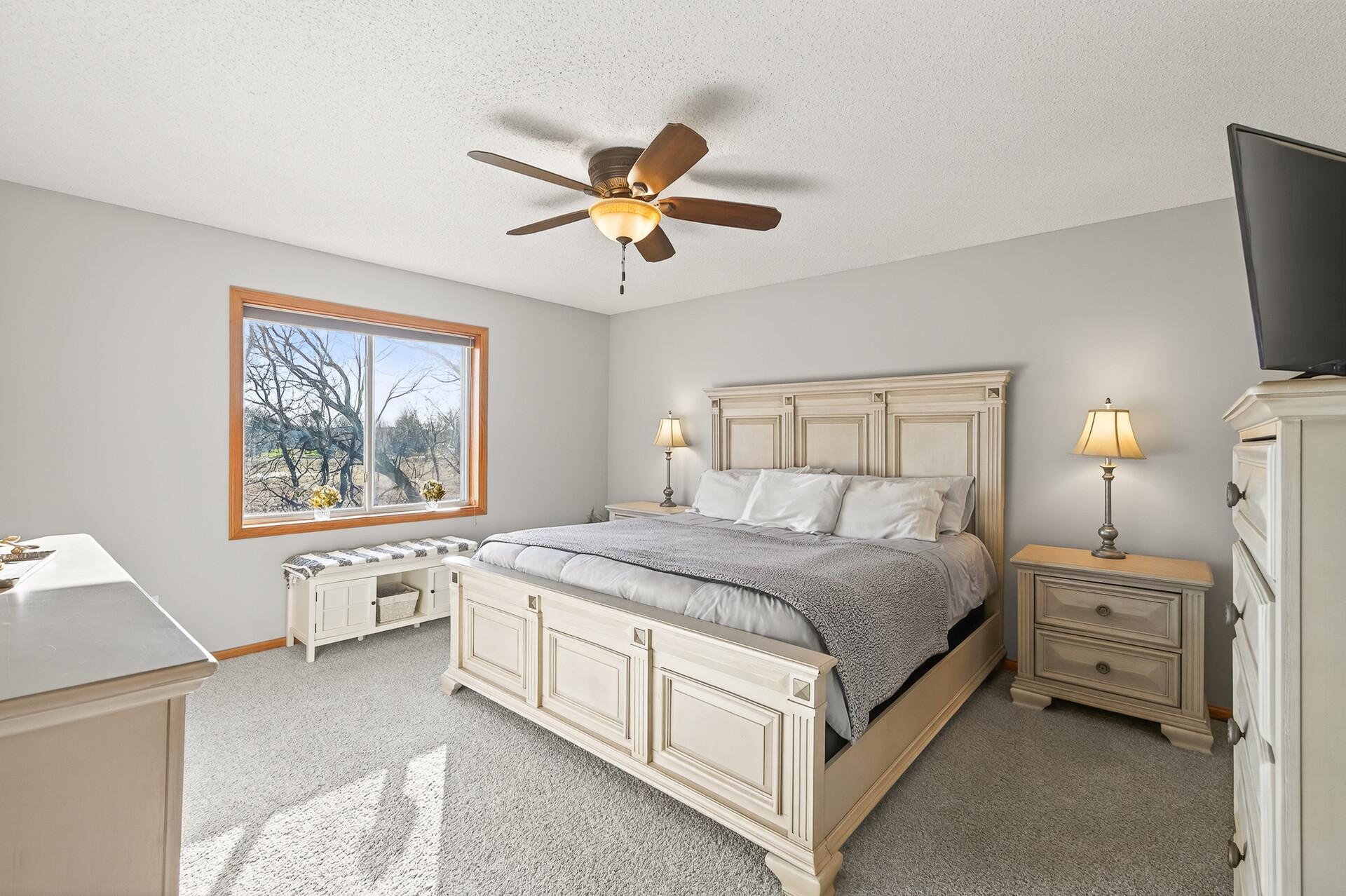 Spacious bedroom with neutral paint, ceiling fan, large window, and comfortable natural light.