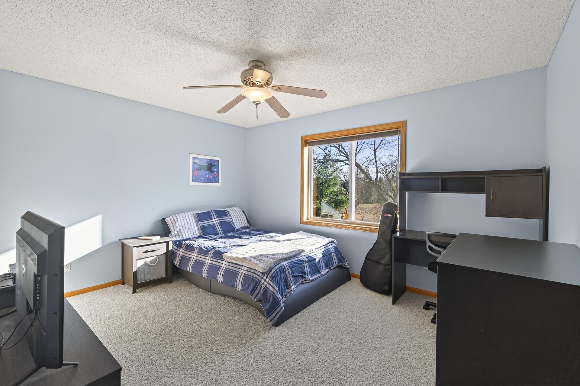 Comfortable secondary bedroom with large window, ceiling fan, and space for a desk or bedroom furniture.