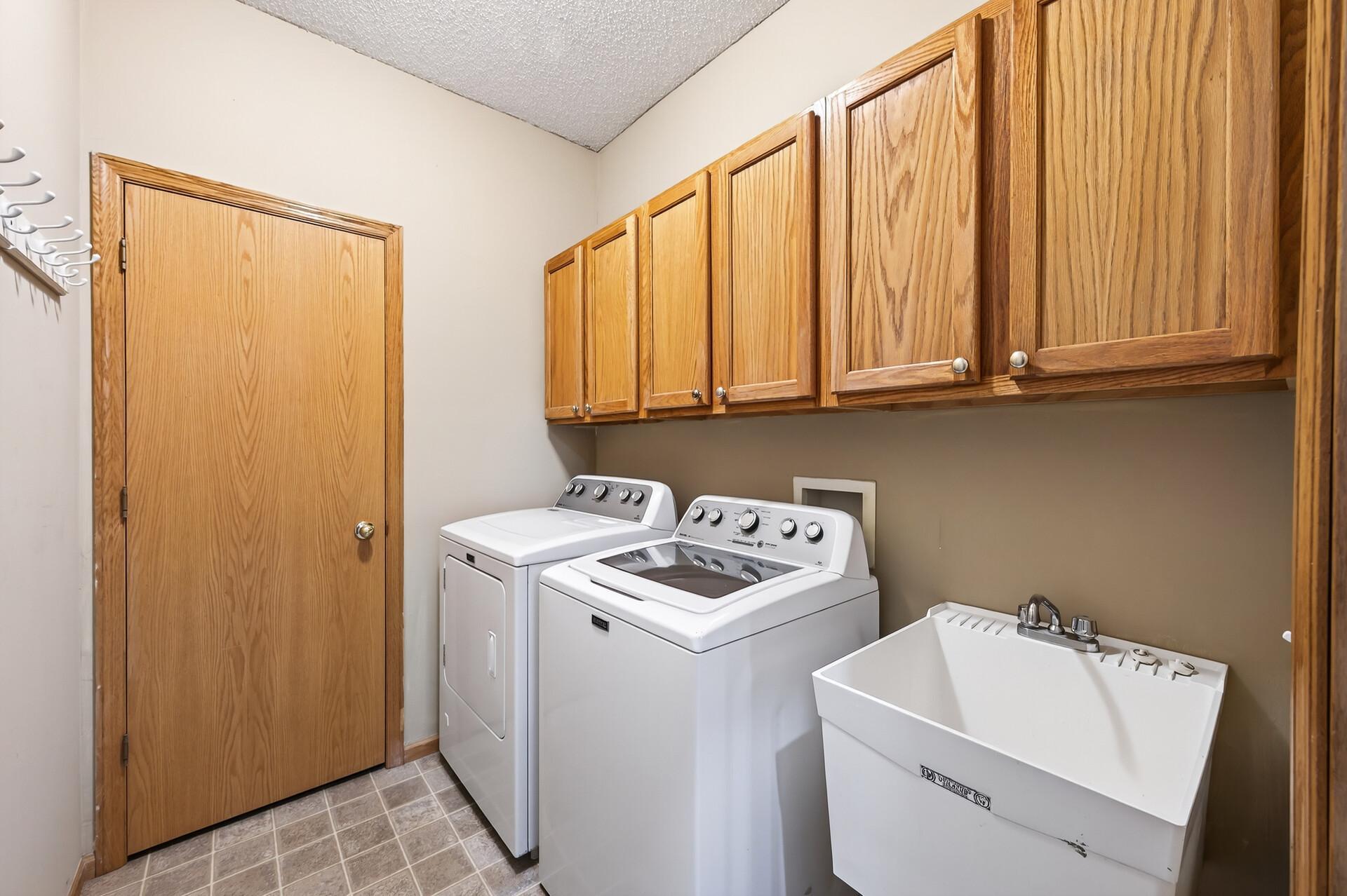 Convenient laundry room with washer, dryer, utility sink, and generous upper cabinet storage.