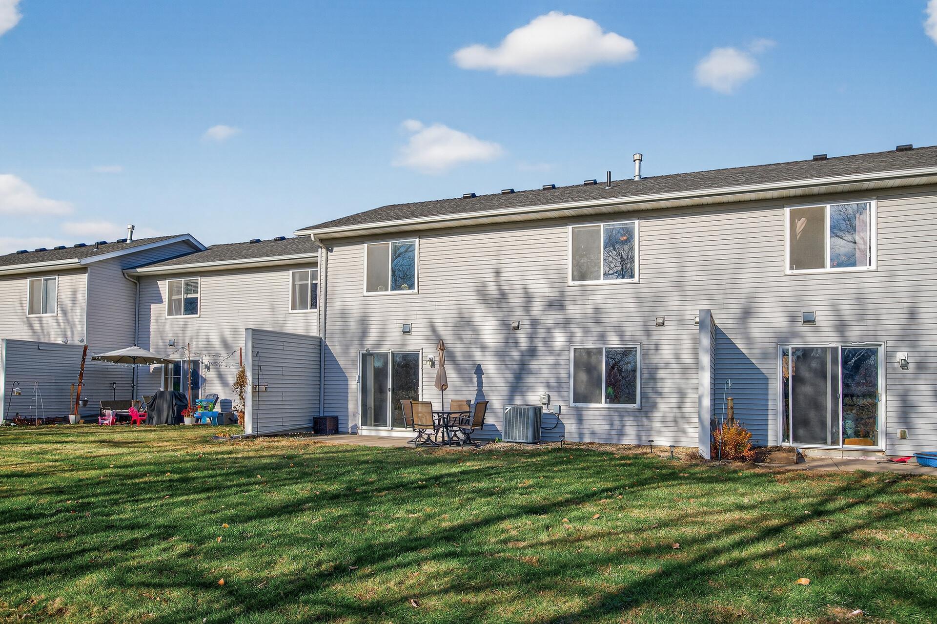 Rear view of the townhome with patio access, vinyl siding, and a peaceful green space backdrop.