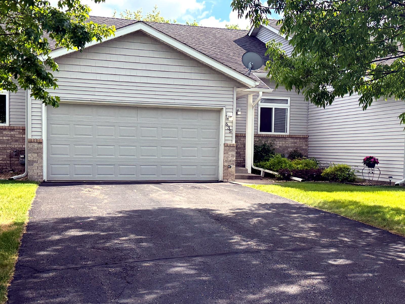 Welcoming front exterior with attached two-car garage, mature trees, and a private front entry.