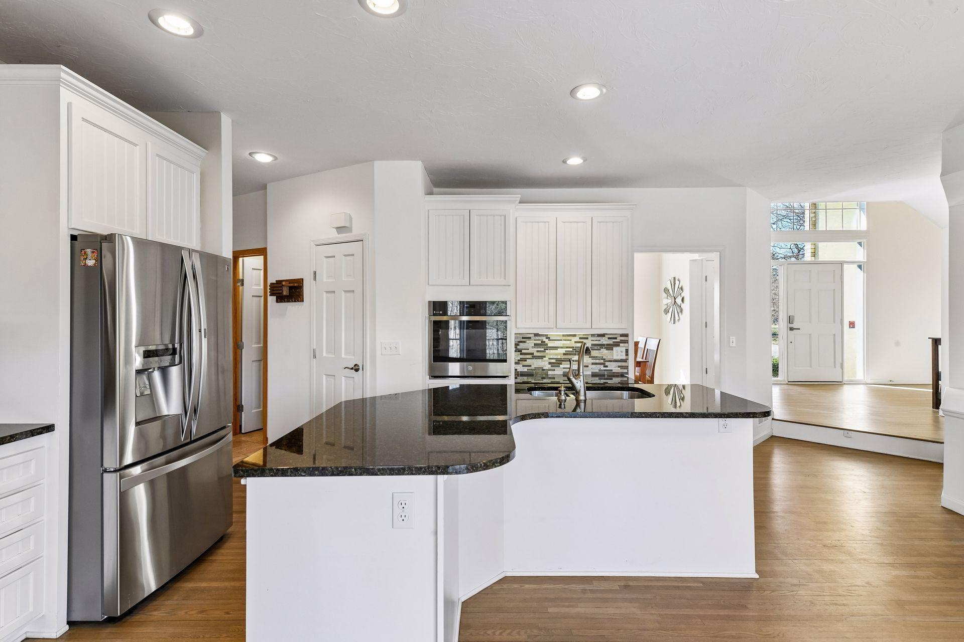 Another great angle of the kitchen highlights its abundance of space, bright white cabinets, unique curved island with dark granite, and the stylish tile backsplash!