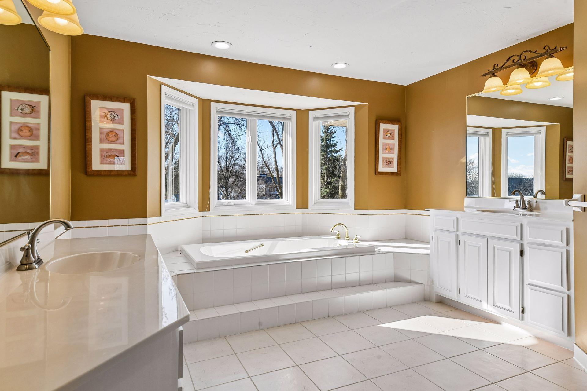 The luxurious primary en suite featuring a sun-drenched soaking tub set into a beautiful bay window. Enjoy dual vanities, crisp white cabinetry, and plenty of space to unwind and relax!