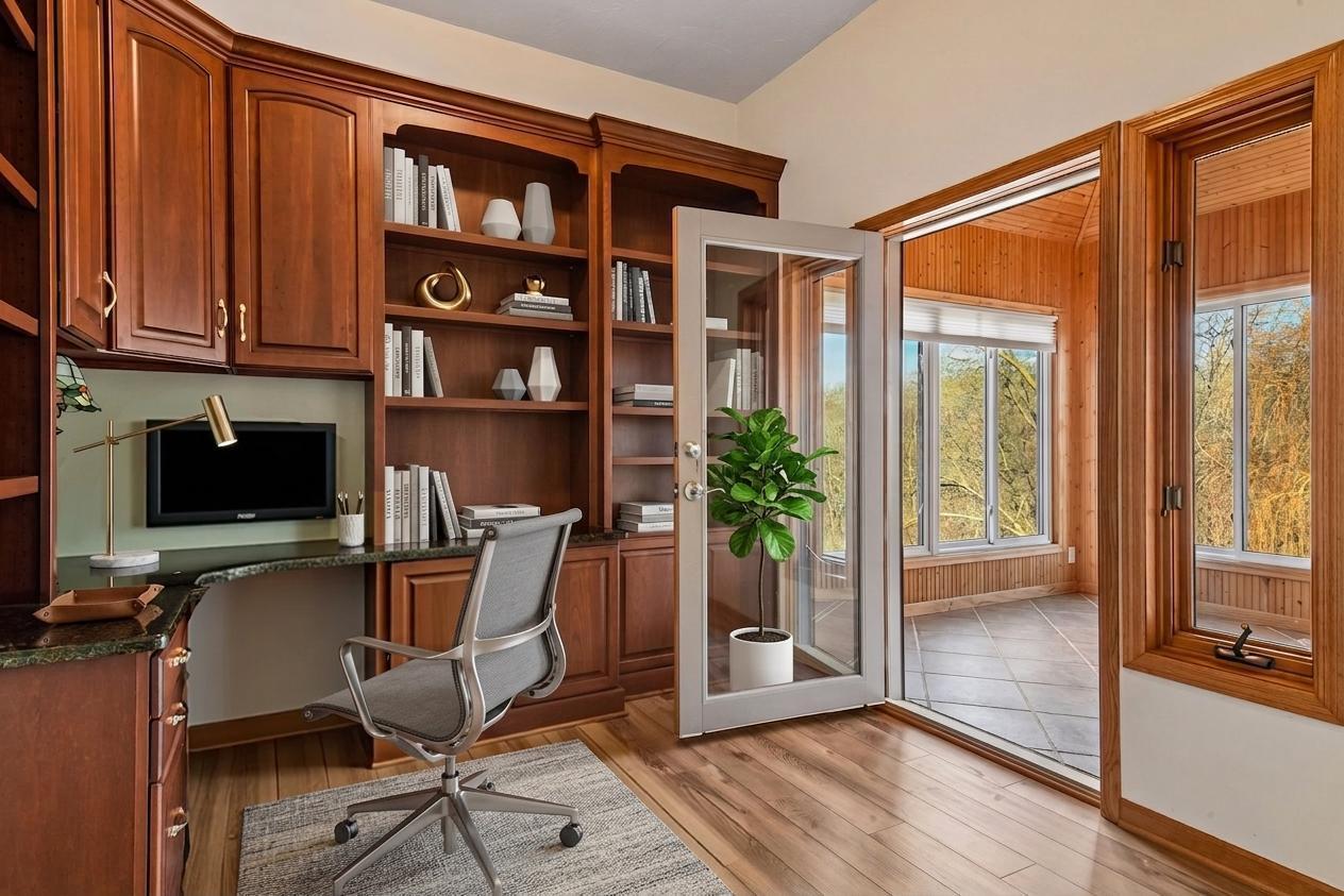 Sophisticated home office featuring rich wood built-ins and a built-in granite desk. A glass door opens directly to the sunroom, providing natural light and a peaceful view while you work! *Virtually staged to show design options.