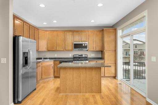 Functional and stylish kitchen with maple cabinetry, stainless steel appliances, center island, ample counter space, and direct access to the maintenance-free deck.