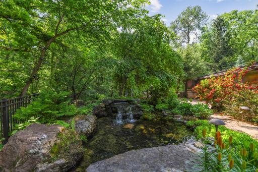 Surrounded by lush ferns and vibrant-colored flowers, the top tier of the back patio water feature has water gently cascading down a mini waterfall.