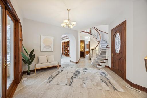 The airy foyer offers a warm welcome with a wall-mounted water feature, abundant natural sunlight, and a beautiful curved staircase.