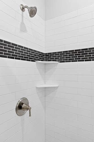 Beautiful walk-in shower with a classic tile surround, contrasting accent tile, and built-in corner shelves for everyday convenience.