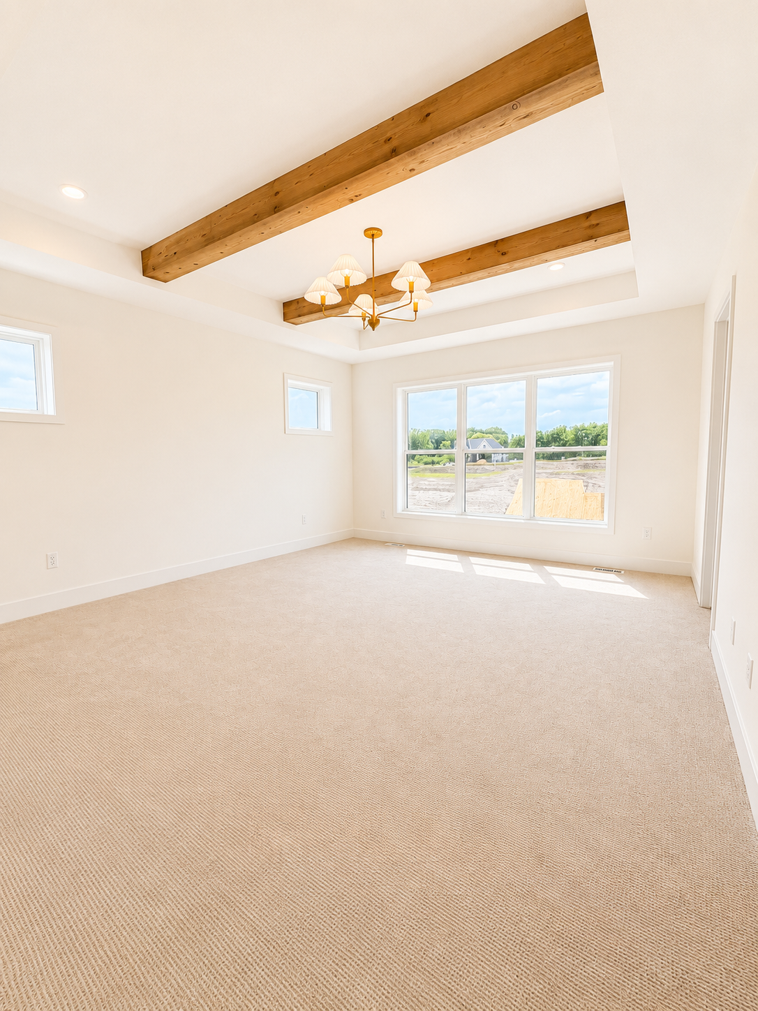 Expansive owner's suite with vaulted ceilings, decorative wood beams, plush carpeting, and abundant natural light.