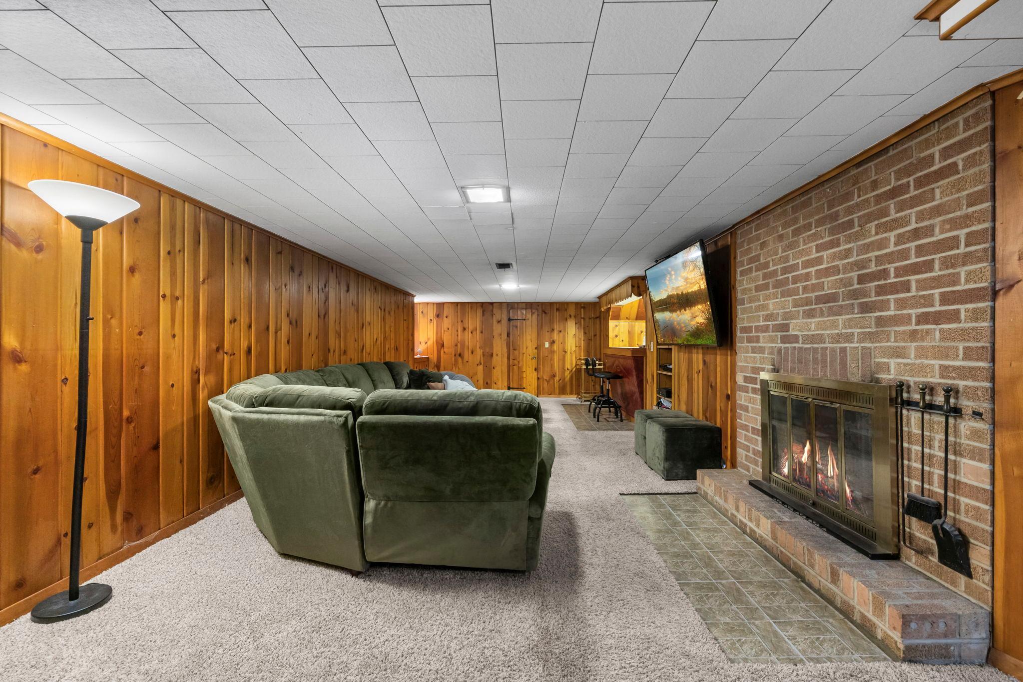 Brick fireplace (wood burning) is capped. Cedar wood wall paneling throughout the basement with storage shelving hidden.