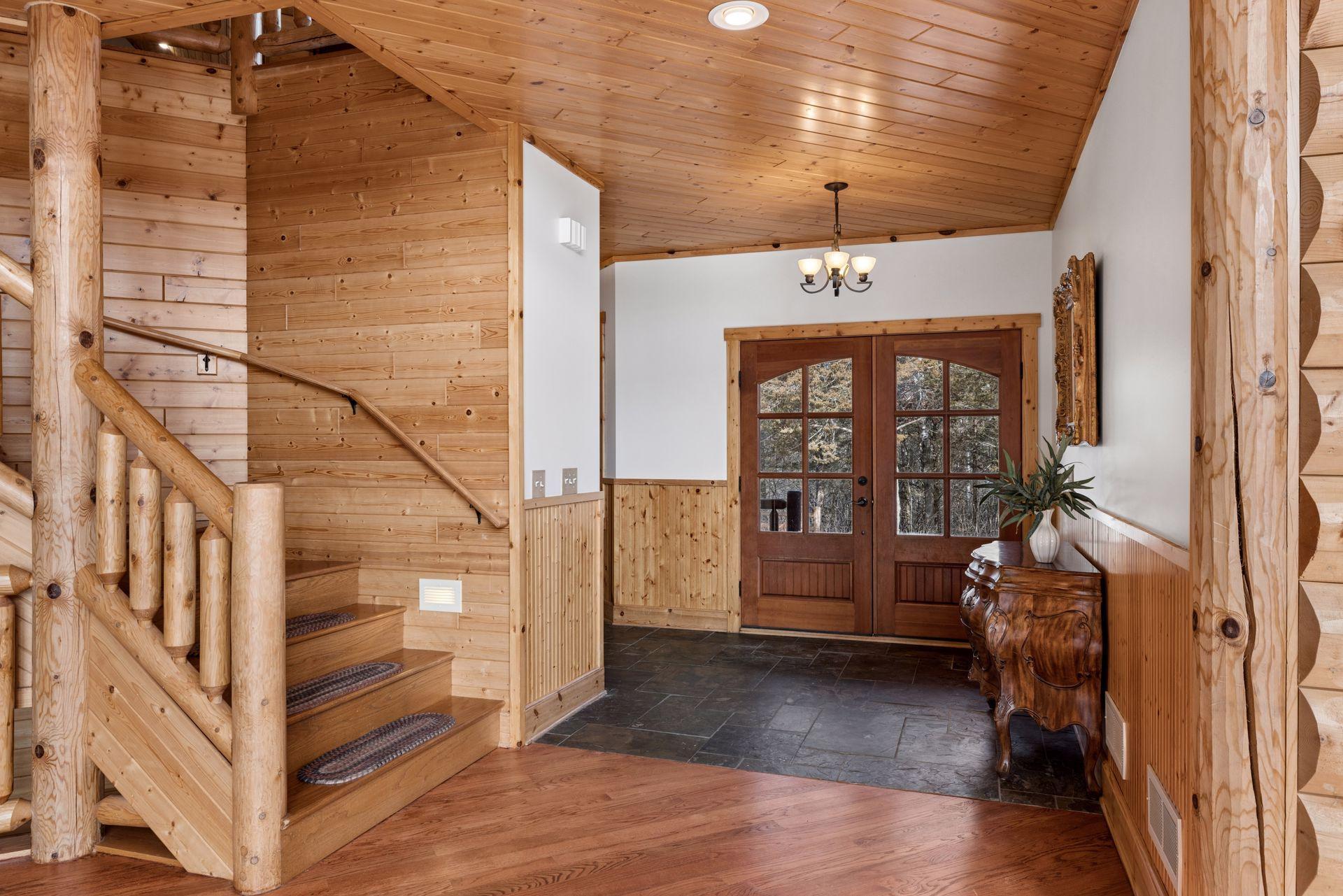 Warm, welcoming foyer with slate flooring, custom woodwork, and log staircase
