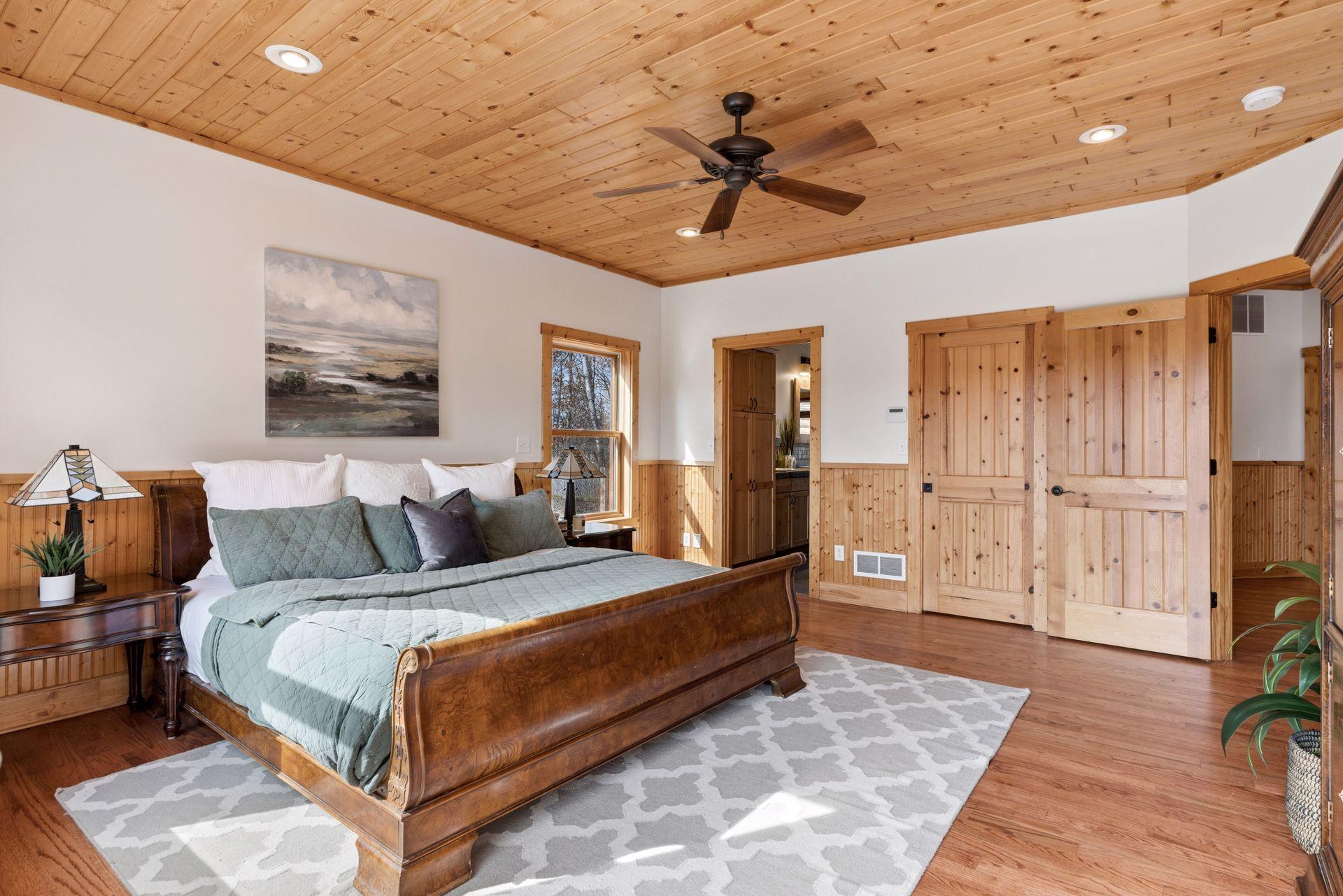 Spacious primary suite with wood ceilings, walk-in closet, private deck access, and serene wooded views