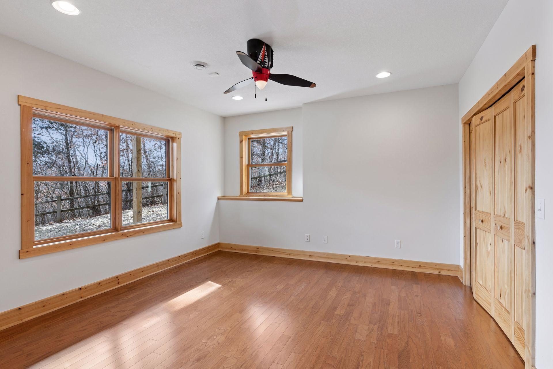 Bright lower-level bedroom with hardwood floors, large windows, built-in shelves and wooded views