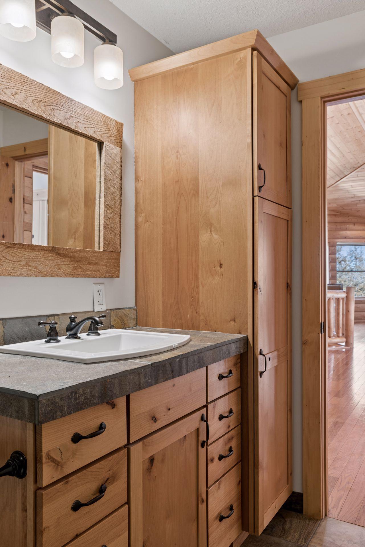 Bathroom vanity with stone countertop, rustic cabinetry, and built-in storage tower
