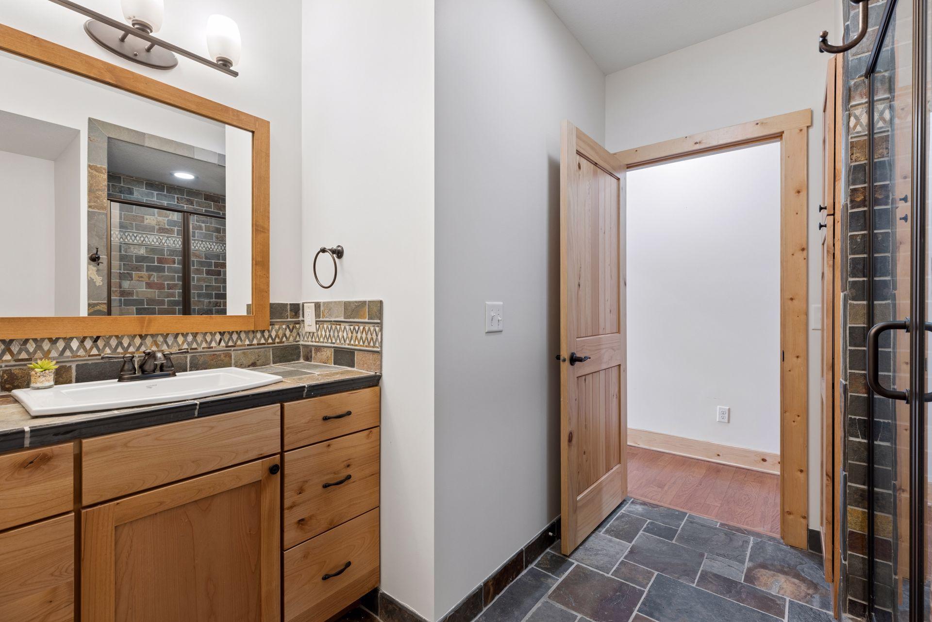 Lower-level bathroom with stone tile flooring, custom vanity, and quality finishes