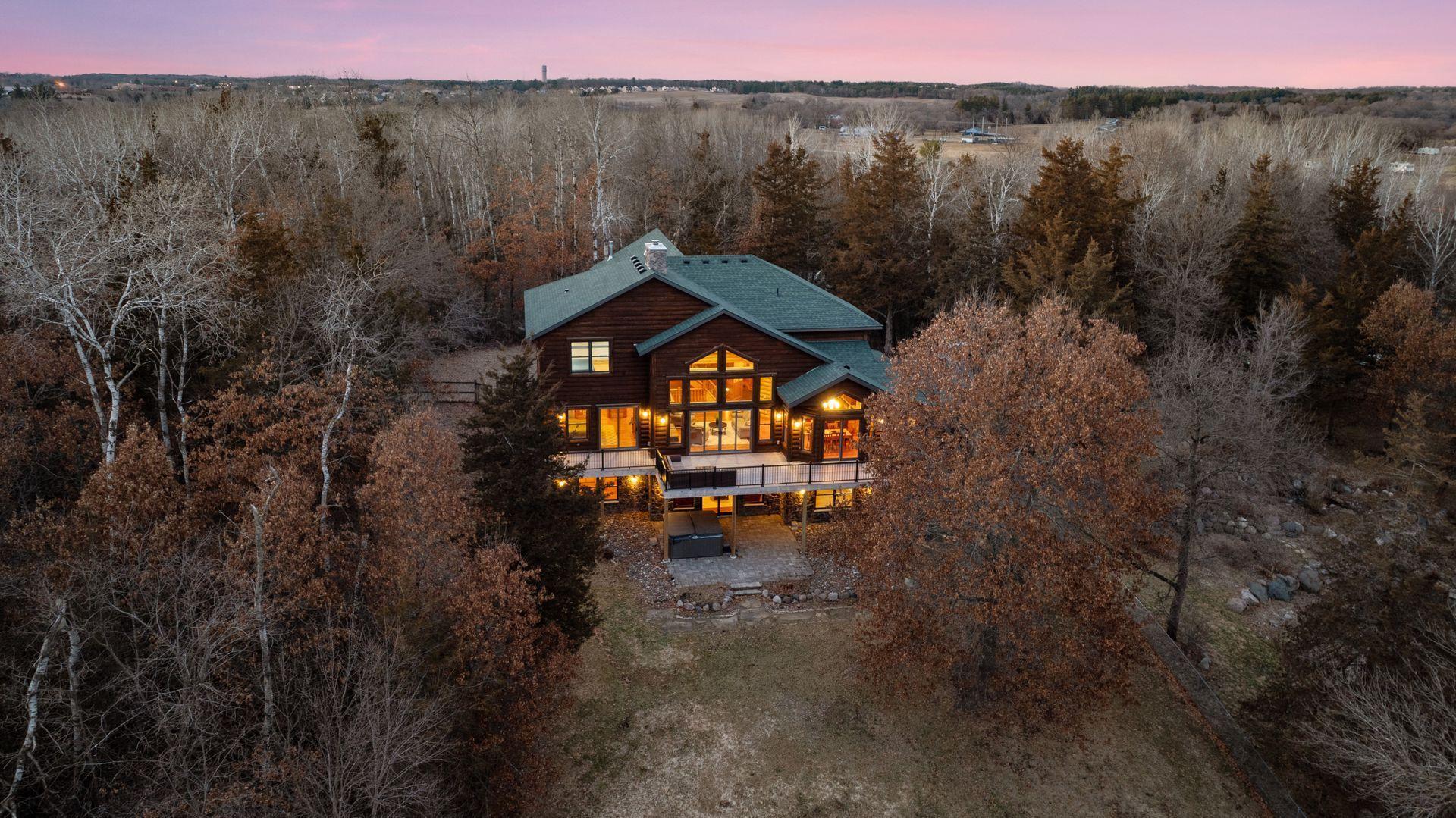 Stunning dusk aerial showcasing the home’s warm glow nestled among mature trees on a private setting