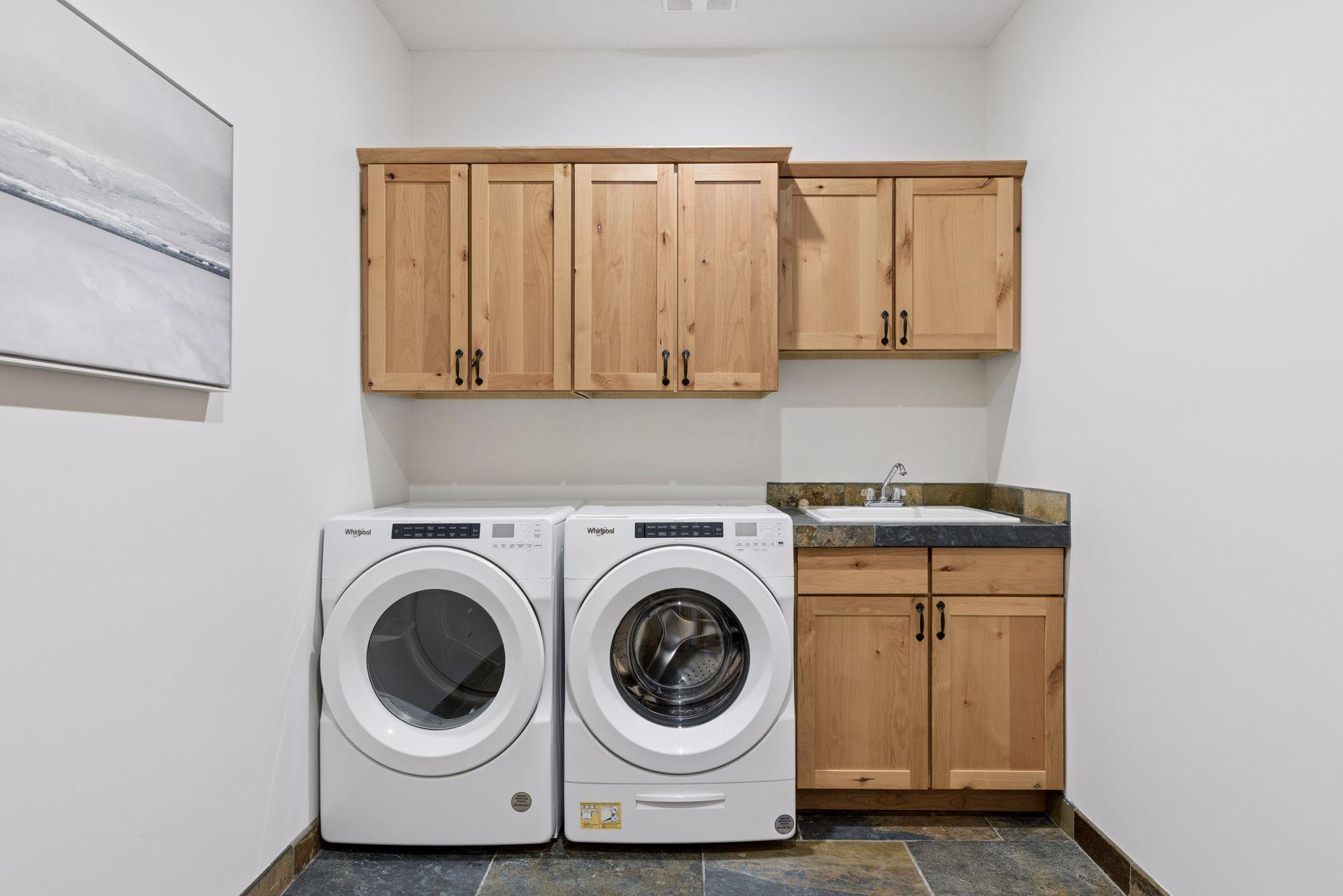 Just steps away from the primary suite, this main level laundry room includes rustic cabinetry and slate floors to match the home's aesthetic, a utility sink, and additional storage.