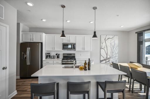Spacious kitchen with large center island, quartz countertops, tile backsplash, white cabinets, pull out trash/recycling cabinet, and the popular stainless steel appliances! *Photo of actual home