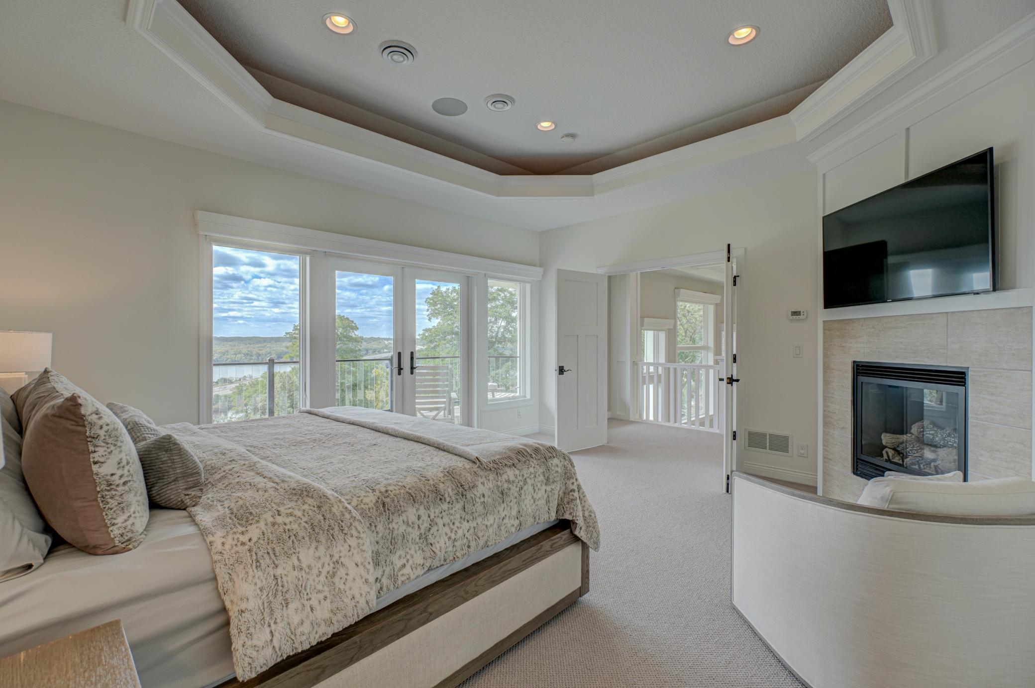 The primary suite is a private sanctuary adorned with a tray ceiling, cozy fireplace, and a private deck showcasing sweeping river views.