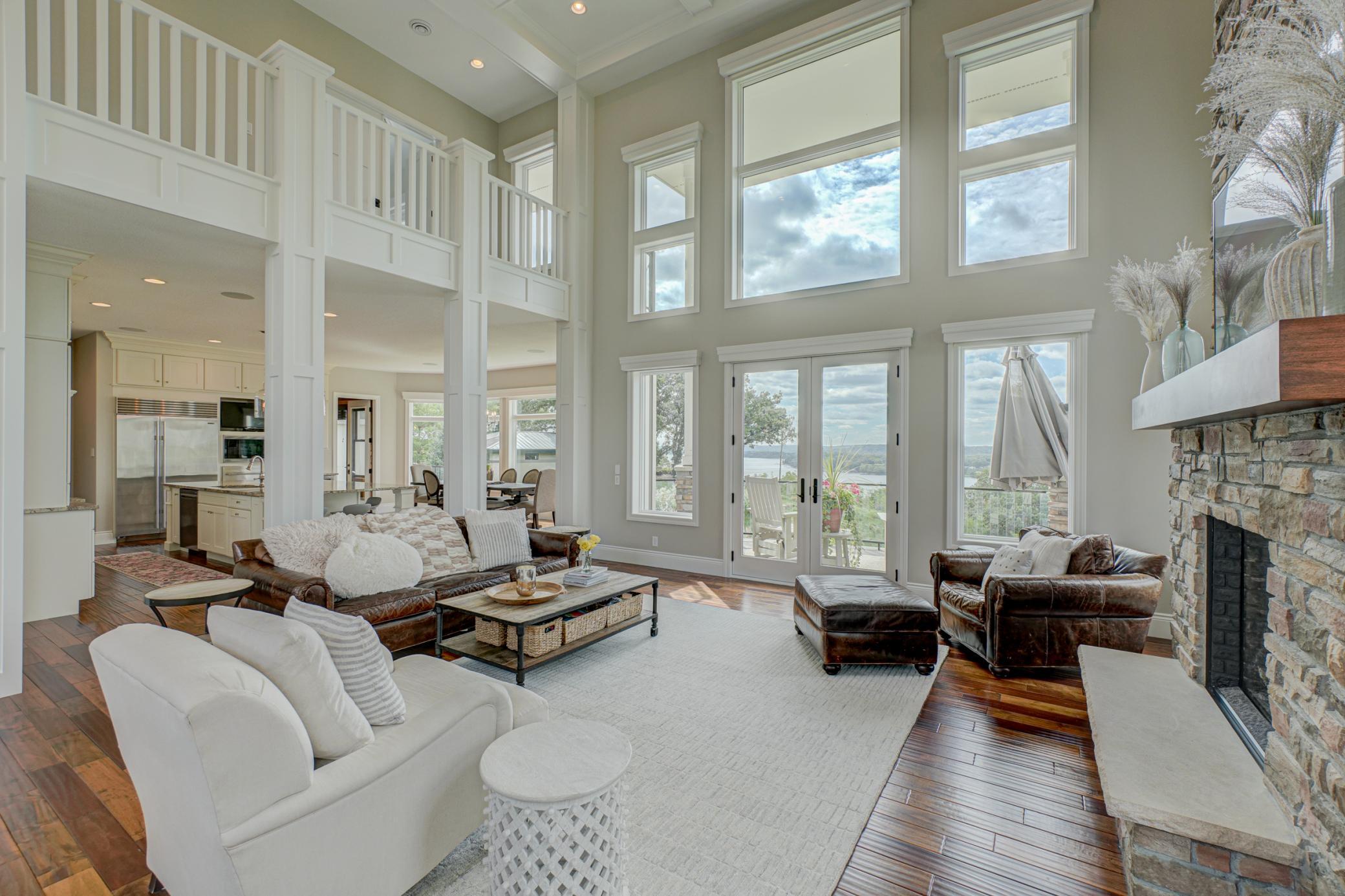 The dramatic two-story great room is the heart of the home, showcasing a striking stone fireplace, coffered ceilings, and an open balcony overlook to the second level. French doors lead to a spacious composite deck, perfect for outdoor entertaining.