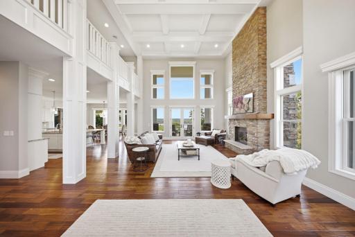 The dramatic two-story great room is the heart of the home, showcasing a striking stone fireplace, coffered ceilings, and an open balcony overlook to the second level. French doors lead to a spacious composite deck, perfect for outdoor entertaining.