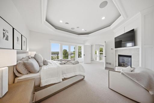The primary suite is a private sanctuary adorned with a tray ceiling, cozy fireplace, and a private deck showcasing sweeping river views.