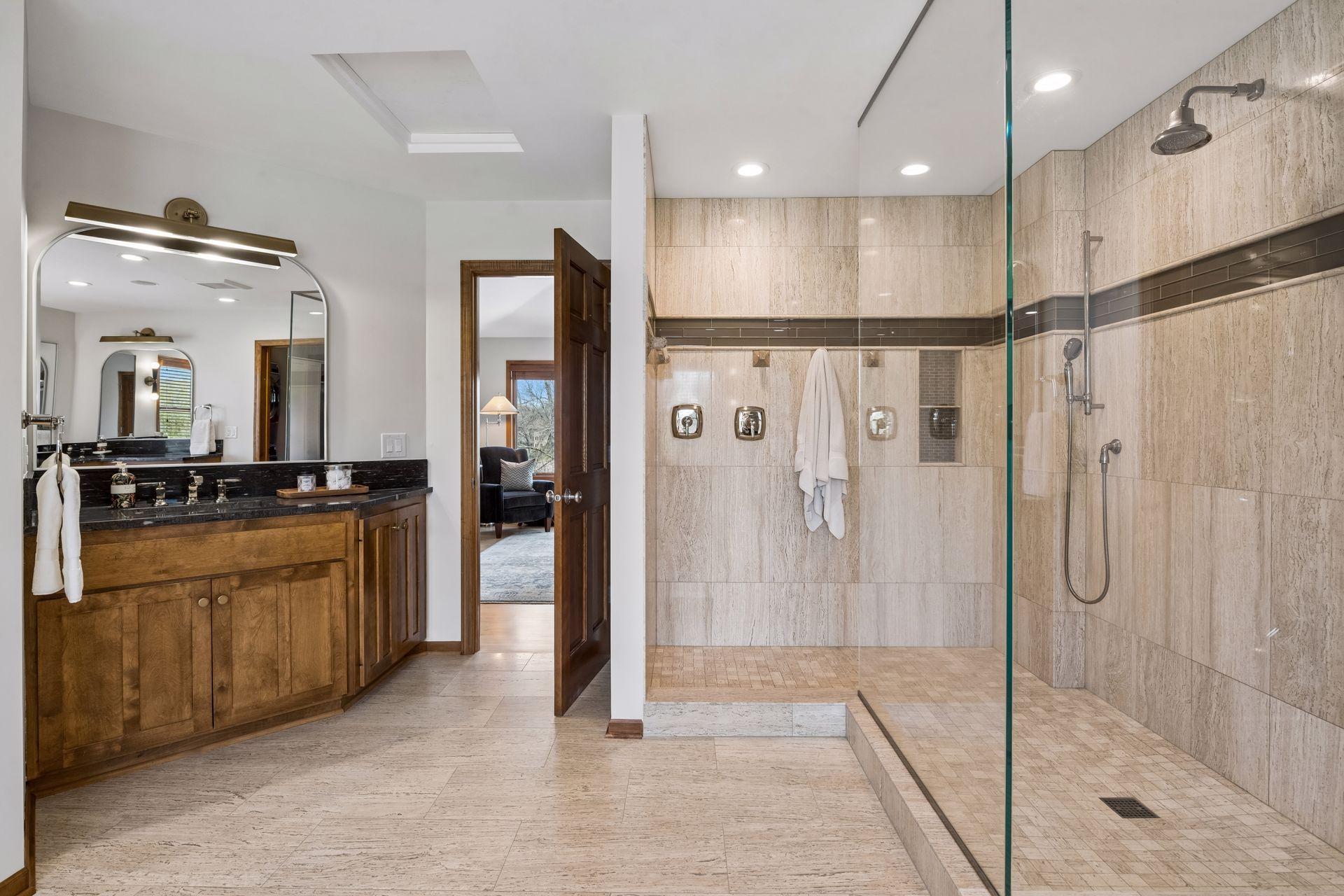 Custom walk-in glass shower with overhead and handheld shower sprays. New granite topped vanity, mirrors and lighting.