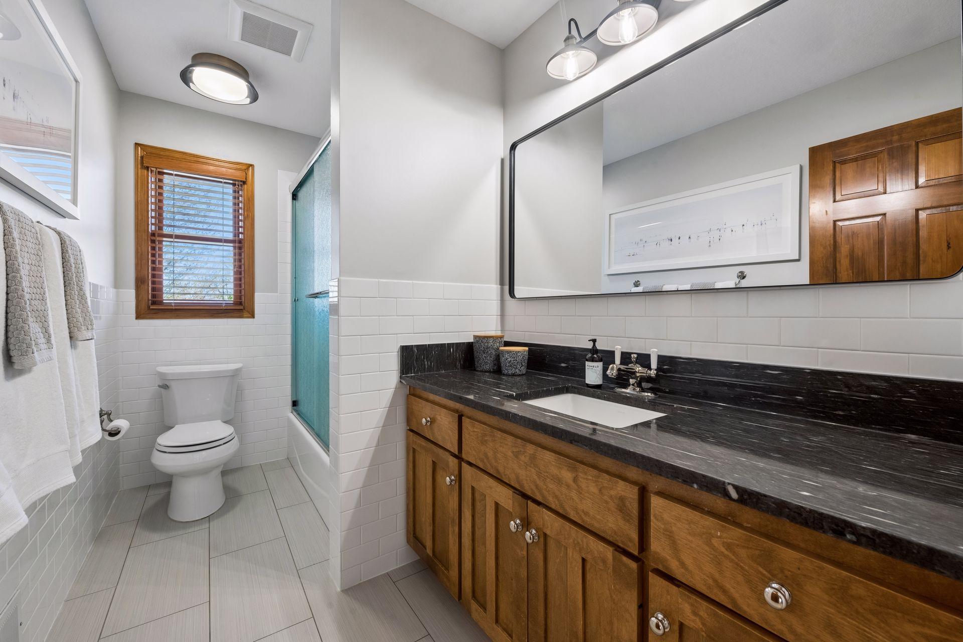 Upper level hall bath with heated floors, tub shower with glass doors and tile surround. Beautiful granite-topped vanity.
