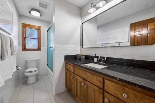 Upper level hall bath with heated floors, tub/shower with glass doors and tile surround. Beautiful granite-topped vanity.