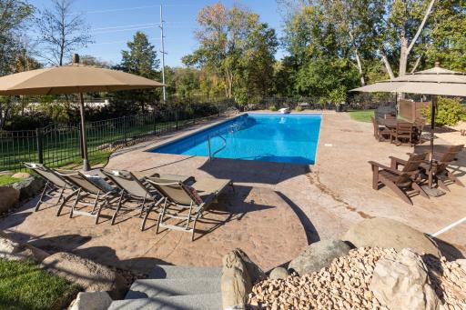 Private backyard oasis with an in-ground swimming pool stamped concrete patio and mature trees.