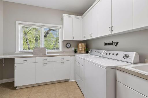Convenient main floor laundry room with an abundance of cabinetry, sink and tile floor.