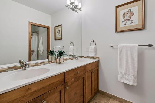Lower level full bath with dual sinks, linen cupboard and tile flooring.