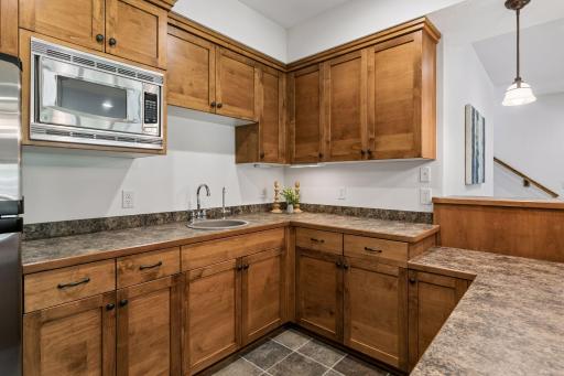 Closer view of the stylish wet bar featuring a refrigerator, microwave, sink, undercabinet lighting and tile flooring. A spacious adjacent storage closet adds even more convenience and functionality.